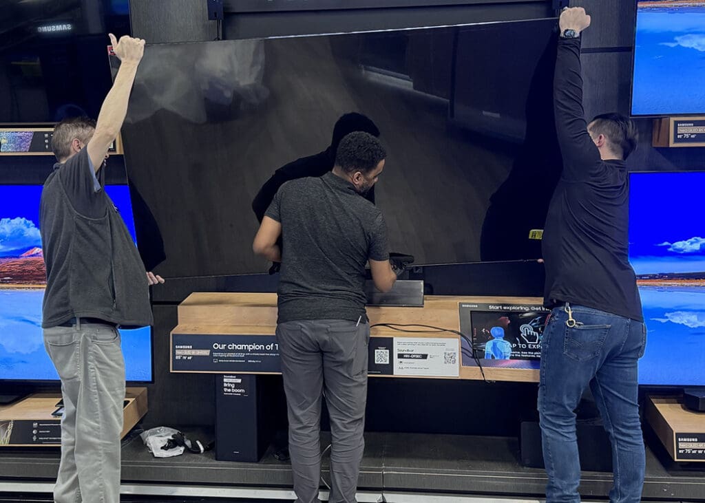 a team of merchandising experts install a tv on a custom wall display